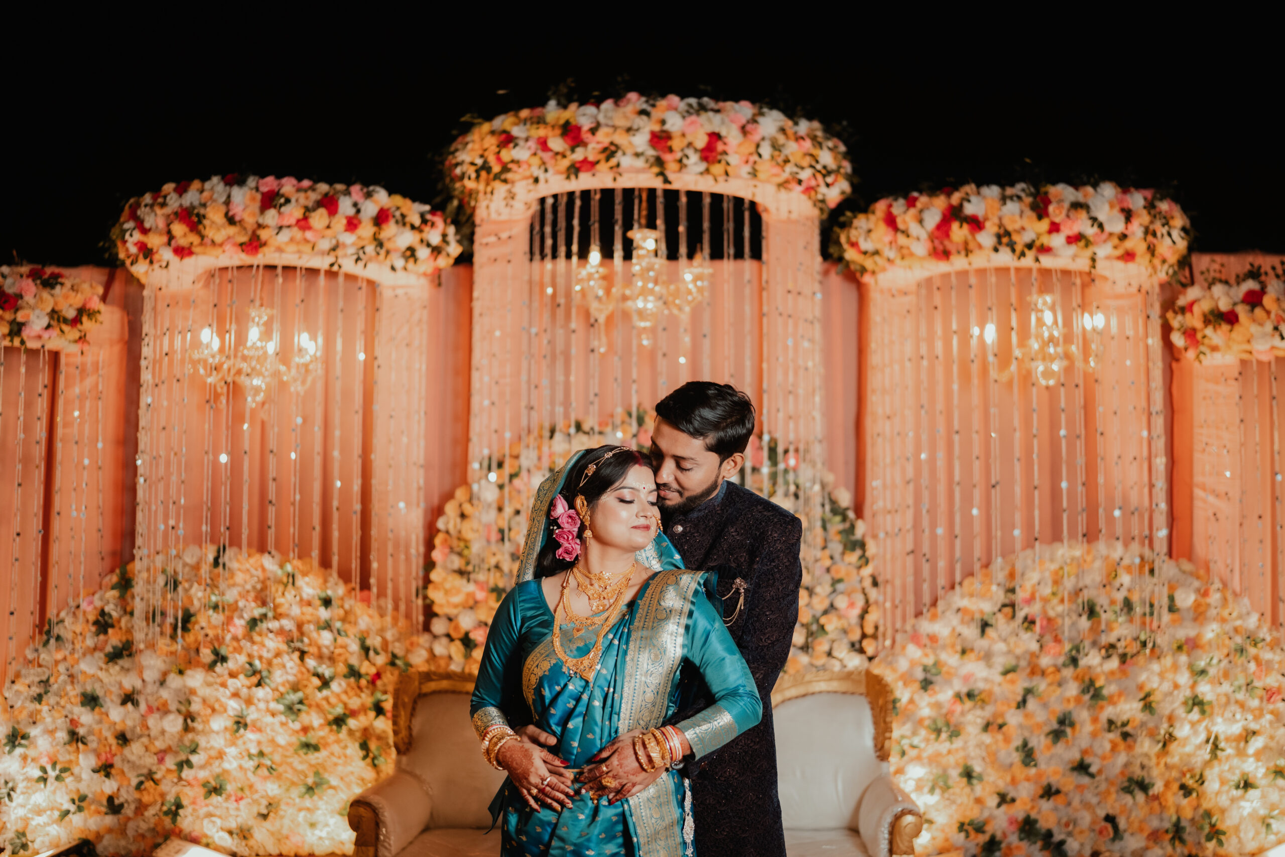 Couple posing together under a floral wedding backdrop