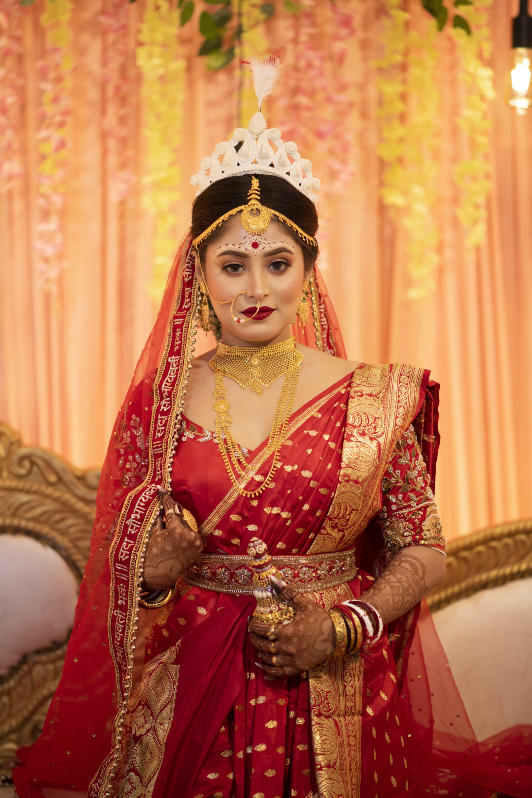 Bengali bride in a red sari against a warm golden wedding backdrop